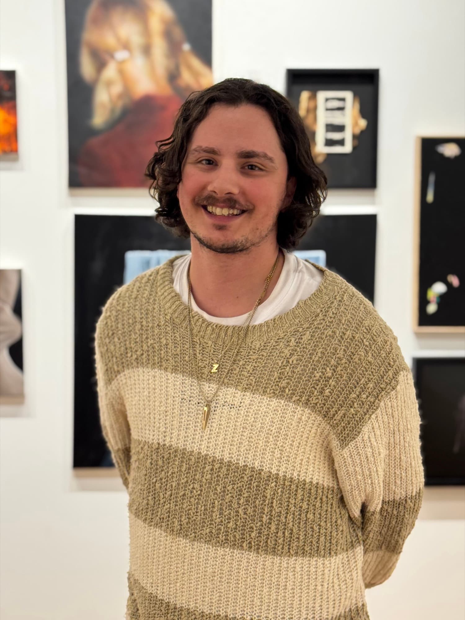 Blake Zigrossi smiles in a striped knit sweater in front of a wall of paintings.